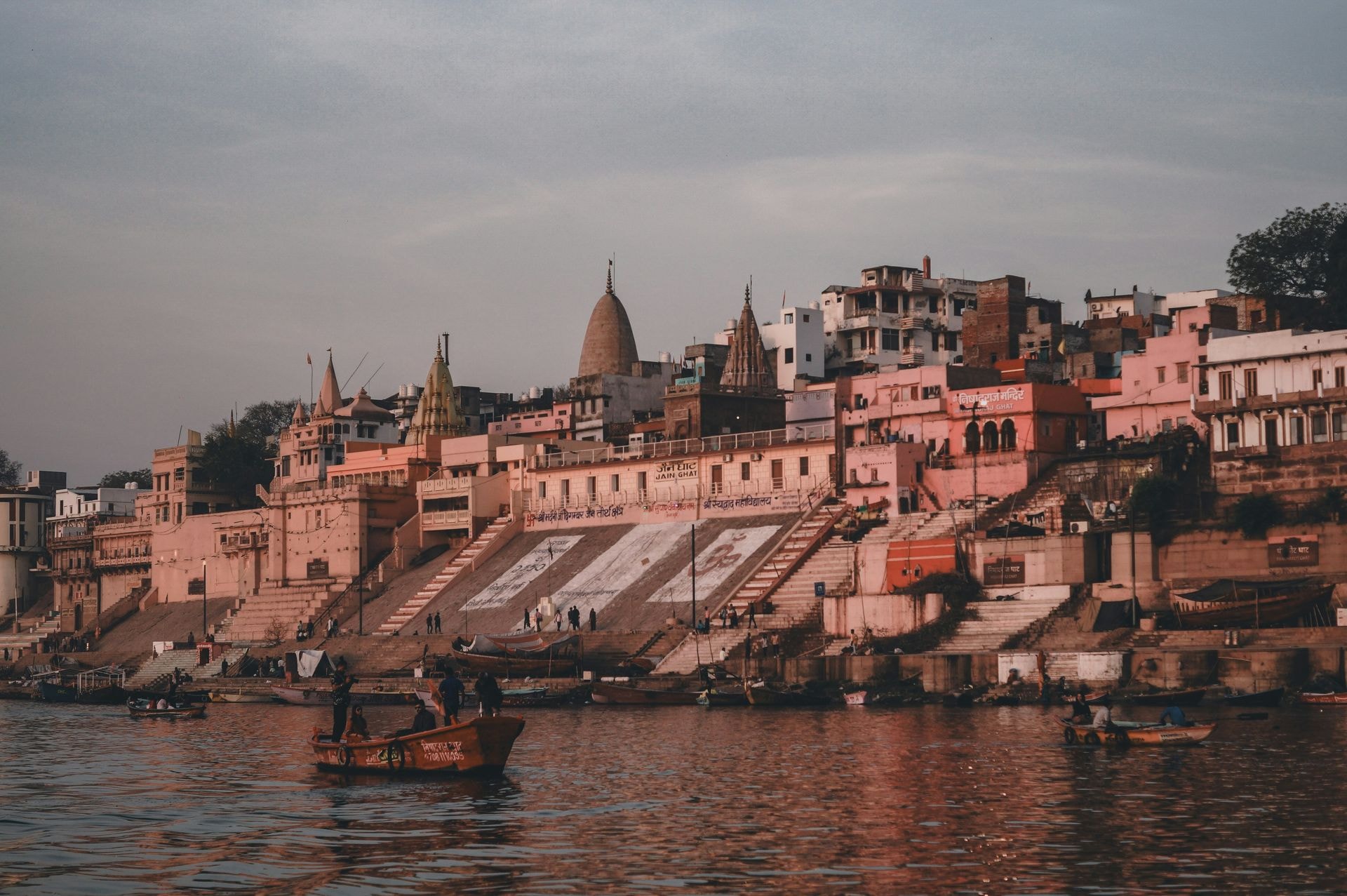 Sunlit riverfront ghats of Varanasi lined with ancient stone palaces and resting wooden boats